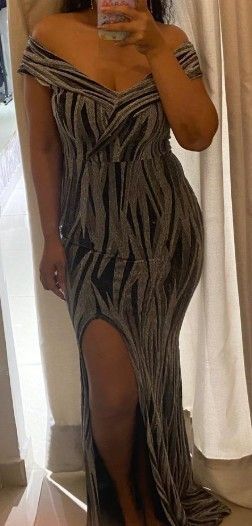 Mujer con un vestido largo hasta el suelo, con hombros descubiertos y una abertura lateral alta, sosteniendo un teléfono