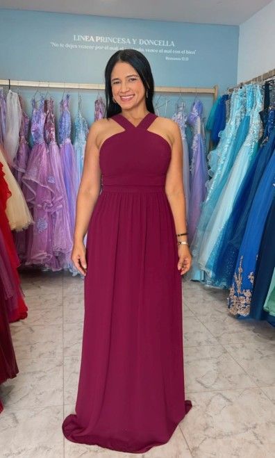 Mujer con un vestido halter color burdeos posando en una tienda de vestidos. Vestidos colgados al fondo.