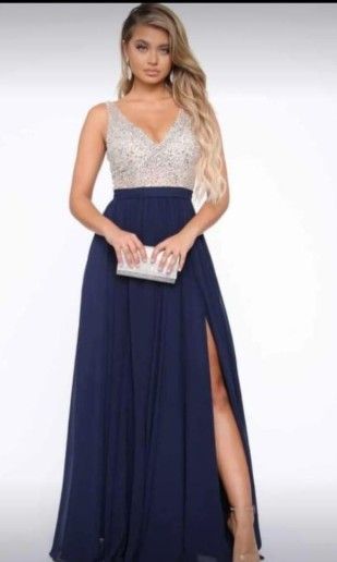 Mujer con vestido azul marino de abertura alta y corpiño con cuentas, sosteniendo un bolso de mano.