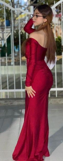 Mujer con vestido rojo de hombros descubiertos, posando al aire libre. Lleva gafas y tiene la mano en la cadera.