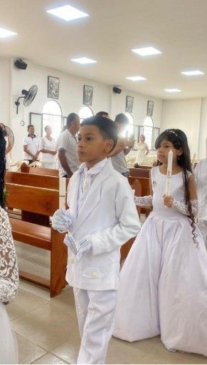Niños vestidos de blanco, algunos con velas, en una iglesia.