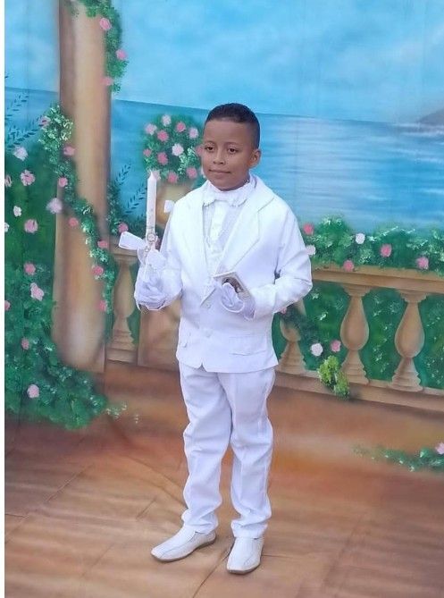 Niño con traje blanco sosteniendo pergaminos, posando frente a un fondo pintado de flores y una escena marina.