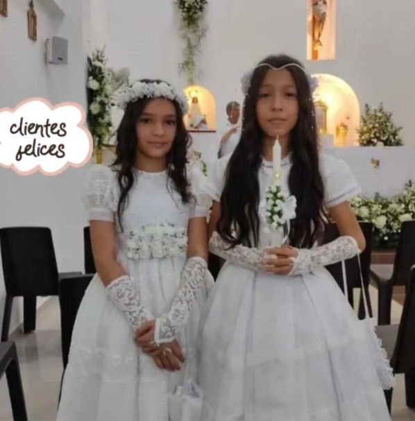 Dos niñas vestidas de blanco sostienen velas dentro de una iglesia.