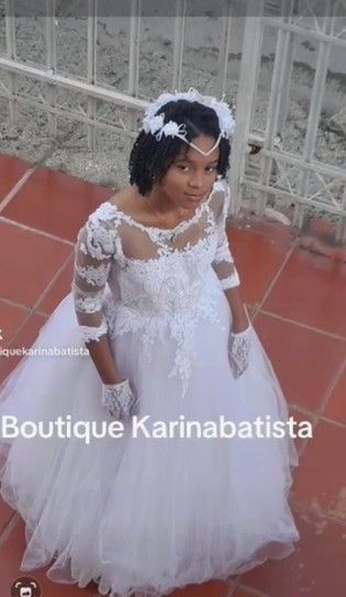 Niña con vestido blanco y velo, mirando hacia arriba. Exterior con ladrillos. Texto: