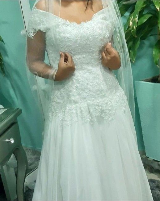 Mujer con vestido de novia blanco de hombros descubiertos y velo, en interiores.