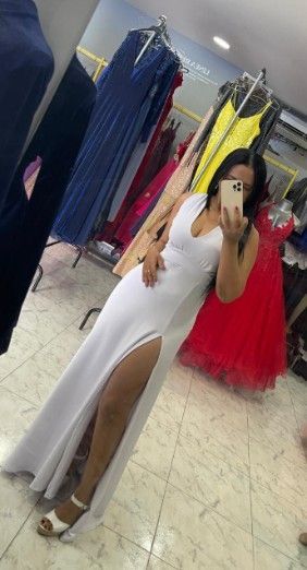 Mujer con vestido blanco de abertura alta, tomándose una selfie en el espejo de una tienda de vestidos.