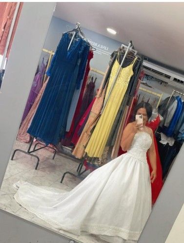 Mujer con un vestido de novia blanco probándoselo frente a un espejo en una tienda de vestidos.