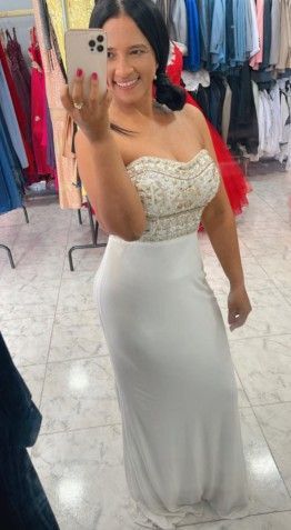 Mujer con un vestido blanco sin tirantes, sonriendo y tomándose una selfie frente al espejo en una tienda de vestidos.