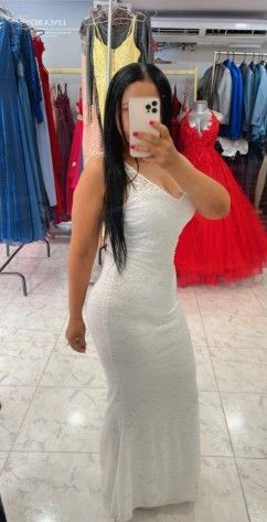 Mujer con vestido blanco de lentejuelas tomándose una selfie en el espejo de una tienda de vestidos.