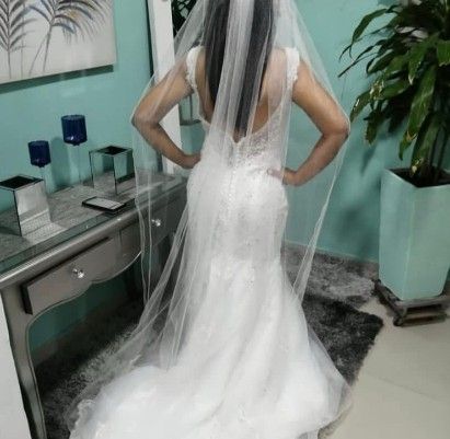 Mujer vestida con un vestido de novia blanco de corte sirena con velo, de pie en el interior con las manos en las caderas.
