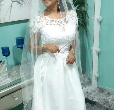 Mujer con vestido de novia blanco con corpiño de encaje, con velo, de pie frente a un espejo.