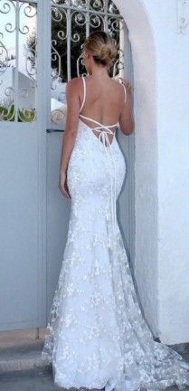Mujer con vestido de novia blanco de encaje con la espalda descubierta, de pie junto a una puerta blanca.