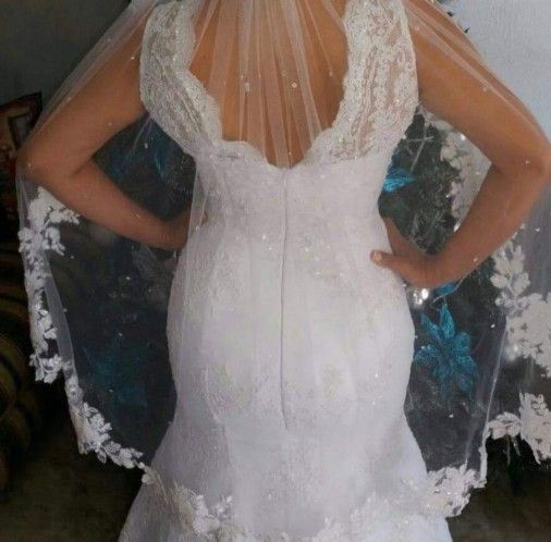 Parte trasera de un vestido de novia blanco con detalles de encaje, espalda baja y velo con ribete floral.