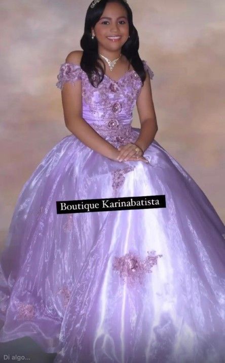 Niña con un vestido de gala lavanda de hombros descubiertos con detalles intrincados, sonriendo, sobre un fondo suave.