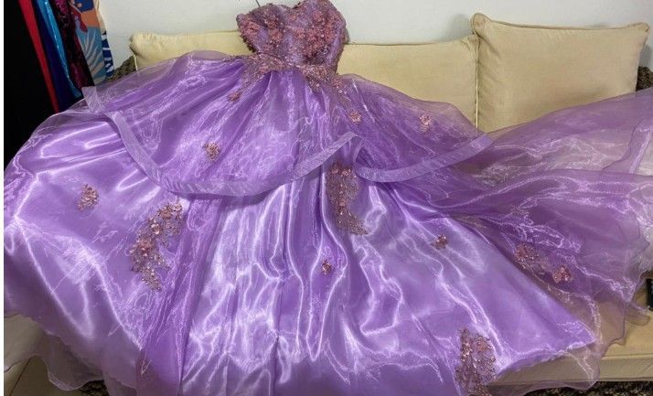 Vestido de gala de organza lavanda sobre un sofá beige; corpiño con adornos florales.