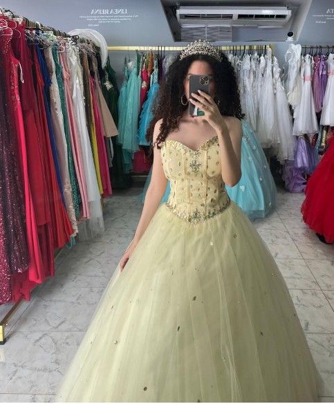 Mujer con un vestido de gala amarillo pálido, luciendo una tiara, tomándose una selfie frente al espejo