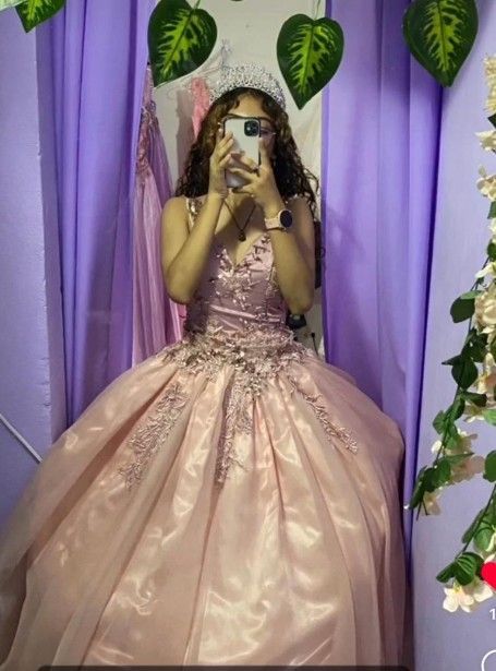 Mujer con vestido de gala rosa y tiara tomándose una selfie frente al espejo.