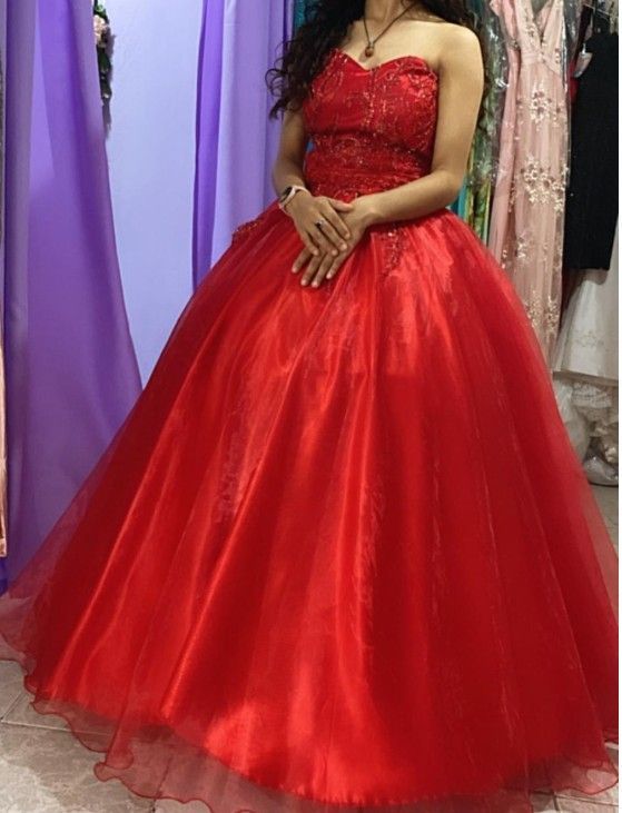 Mujer con un vestido de gala rojo sin tirantes, con las manos entrelazadas, en una tienda de ropa.