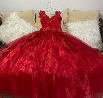 Vestido de gala rojo colgado en una percha, sobre un fondo neutro, con almohadas blancas y mullidas.