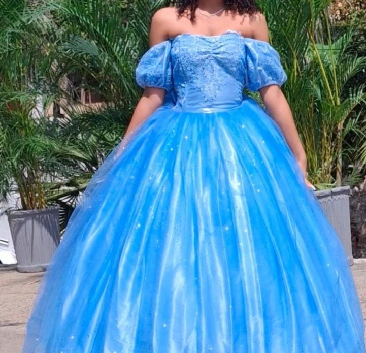Mujer con un vestido azul claro de hombros descubiertos posando al aire libre.
