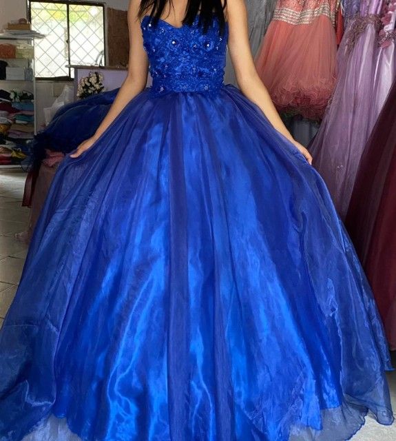 Mujer con un vestido de gala azul real con corpiño de cuentas, sosteniendo la falda.