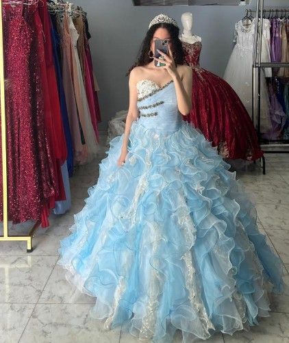 Mujer con un vestido de gala azul claro, tomándose una selfie frente al espejo en una tienda de vestidos.