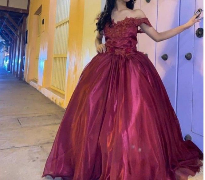 Mujer con vestido rojo de hombros descubiertos posa cerca de una puerta; ambiente nocturno.