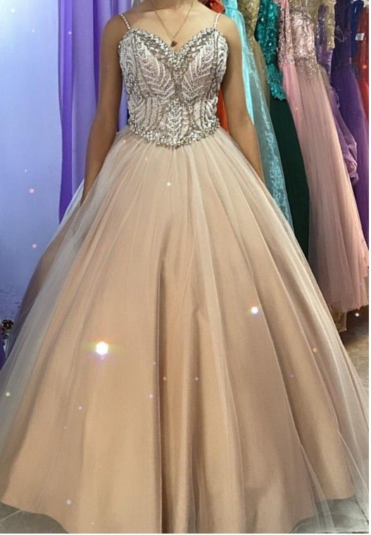 Niña con un vestido de gala color canela con corpiño de cuentas, de pie en una tienda de vestidos.