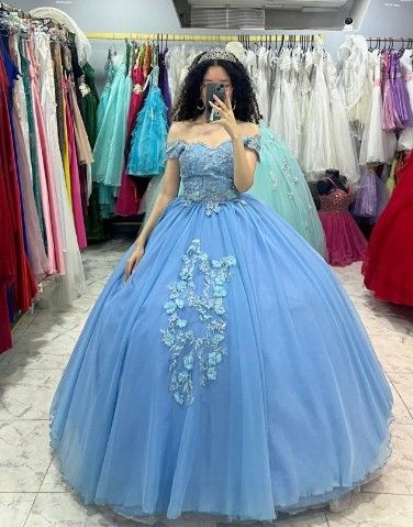 Mujer con vestido de gala azul claro con hombros descubiertos, de pie en una tienda de novias, tomandose una selfie
