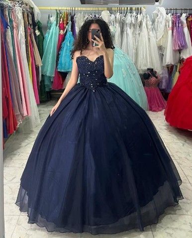 Mujer con un vestido de gala azul oscuro con cuentas, tomándose una selfie en una tienda de vestidos.