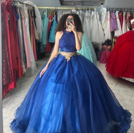 Mujer con un vestido de gala azul real con corpiño de lentejuelas, sosteniendo un teléfono, en una tienda de vestidos.