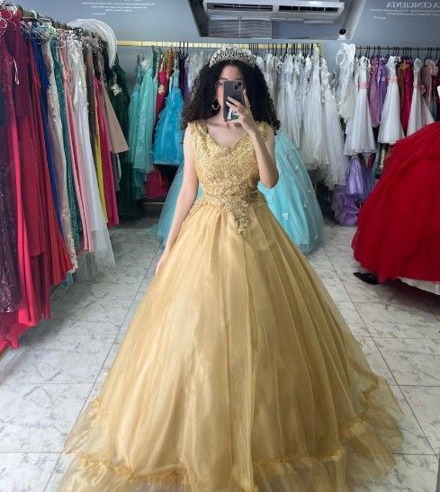 Mujer con vestido de gala dorado, sosteniendo un teléfono, en una tienda de vestidos.