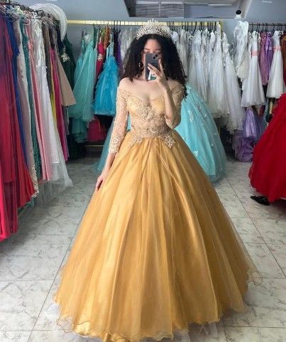 Mujer con un vestido de gala dorado y una corona, tomándose una foto en una tienda de vestidos.