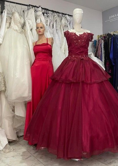 Vestido de gala rojo sobre un maniquí en una tienda de novias, otros vestidos colgados al fondo.