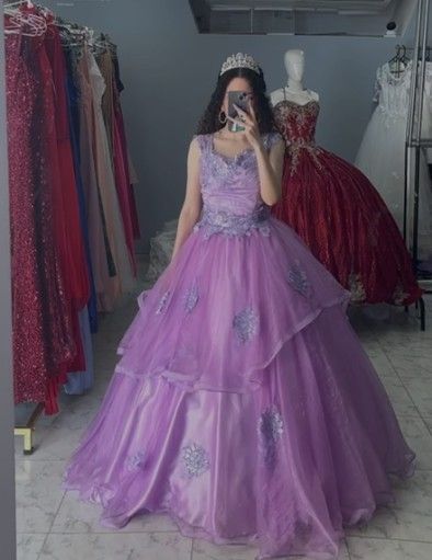 Mujer con un vestido de gala color lavanda y una tiara, tomándose una selfie frente al espejo en una tienda de vestidos.