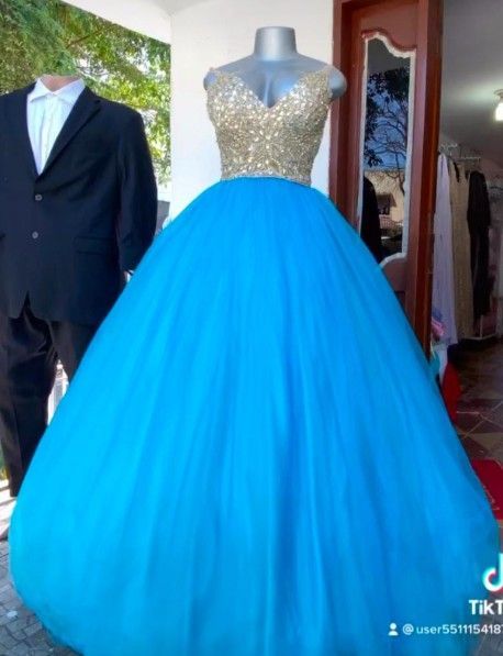 Vestido de gala azul con corpiño dorado sobre un maniquí, junto a un traje negro.