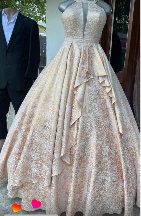 Vestido formal color champán con escote halter y falda amplia, exhibido en un maniquí.