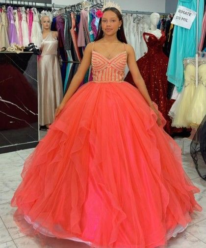 Adolescente con vestido de gala color coral en una tienda de vestidos, posando con una tiara.