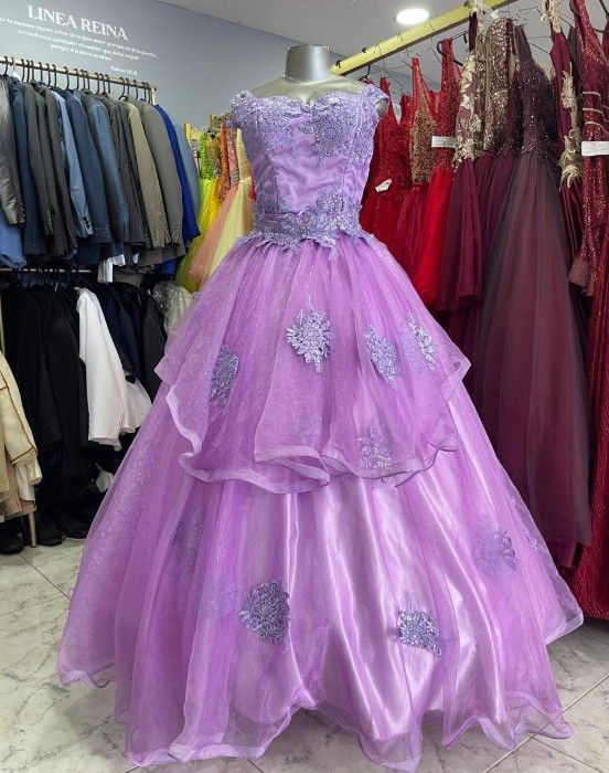 Un vestido de gala de color lila claro, con corpiño de encaje y falda de volantes, sobre un maniquí en una tienda de vestidos