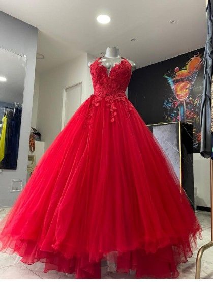 Vestido de gala rojo sobre un maniquí, con corpiño detallado y falda de tul amplia, exhibido en una boutique.