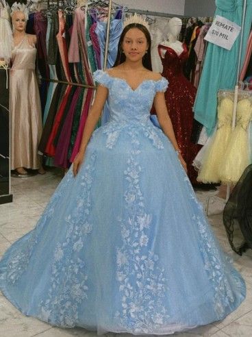 Niña con un vestido azul claro de hombros descubiertos con detalles florales, de pie en una tienda de vestidos.