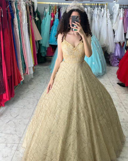 Mujer con vestido de gala dorado, sosteniendo un teléfono, en una tienda de vestidos.