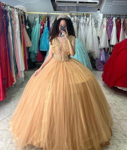 Mujer con vestido de gala dorado, posando en una tienda de vestidos, rodeada de vestidos coloridos.