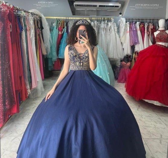 Mujer con un vestido de gala azul marino con corpiño de cuentas, tomándose una selfie en una tienda de vestidos.