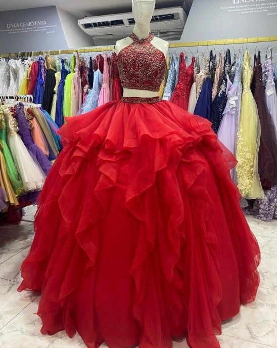 Vestido de gala rojo de dos piezas con corpiño bordado con cuentas y falda con volantes en capas, expuesto en una tienda