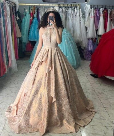 Mujer con un brillante vestido dorado sosteniendo un teléfono, posando en una tienda de vestidos.