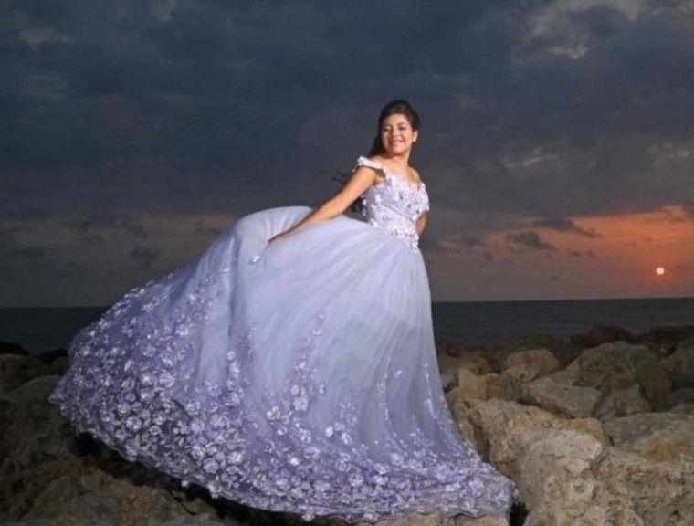 Mujer con vestido lavanda posa sobre rocas cerca del océano al atardecer.