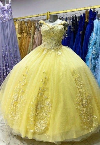 Vestido de gala amarillo con hombros descubiertos y detalles de encaje floral, expuesto en una tienda de vestidos