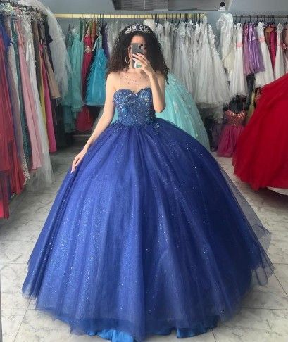 Mujer con un vestido de gala azul sin tirantes y con corpiño de cuentas, de pie en una tienda de vestidos,