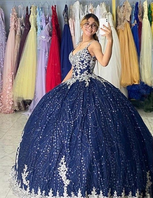 Mujer con vestido de gala azul marino, tomándose una selfie. Vestidos colgados al fondo.